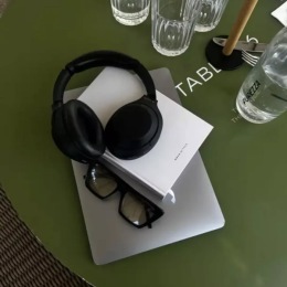 a laptop headphones book sunglasses and drinking glasses on a green table